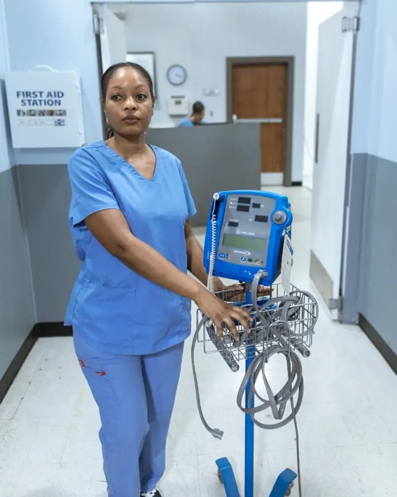 A nurse standing with a patient monitor in a hospital corridor