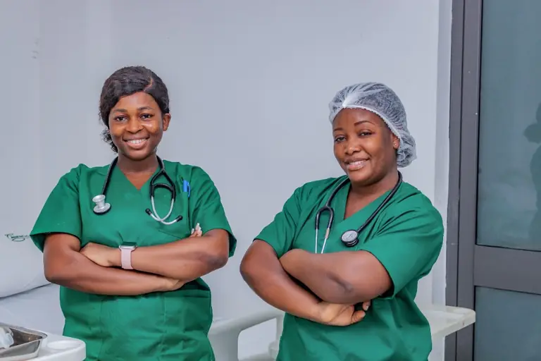 Two nurses in green scrubs standing side by side with arms folded